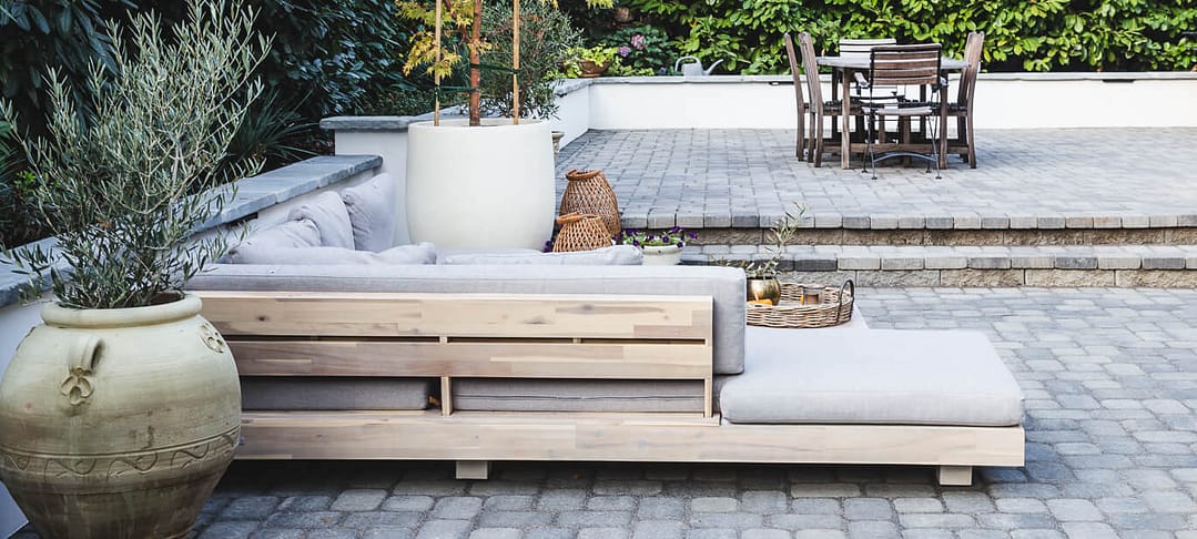 Large patio with paver flooring and retaining walls with outdoor furniture and large potted plants