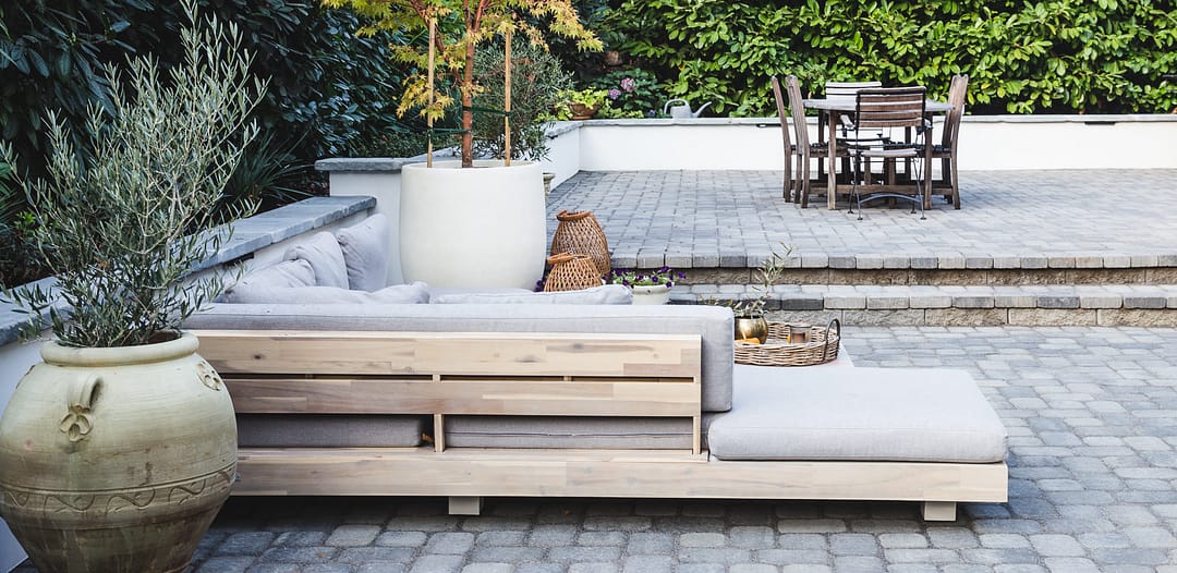 Large patio with paver flooring and retaining walls with outdoor furniture and large potted plants