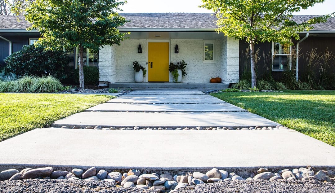 Concrete paver walkway with river rocks between and grass alongside