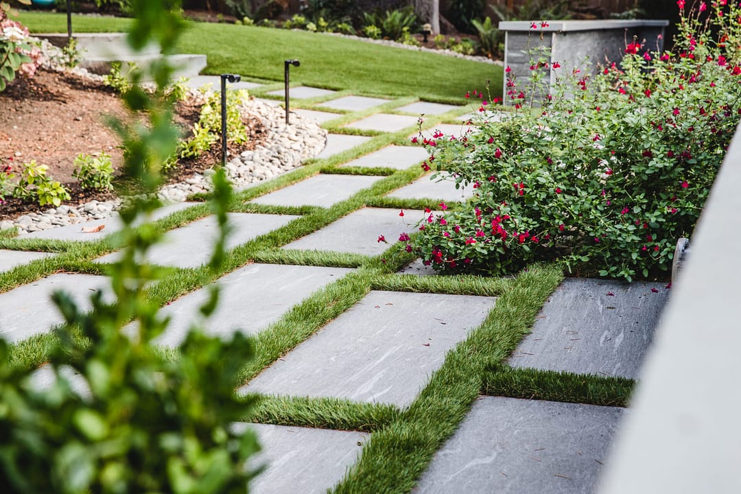 Rectangular stone pavers surrounded by lush green grass and plants