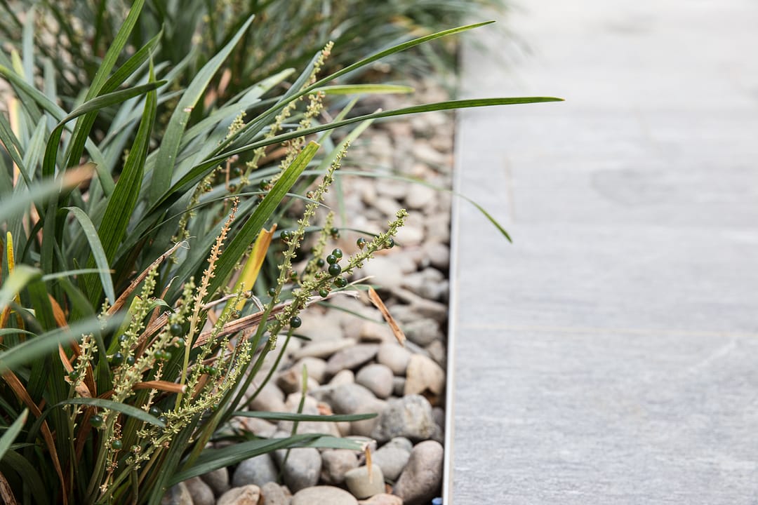Edge of concrete walkway with river rock and grass along side