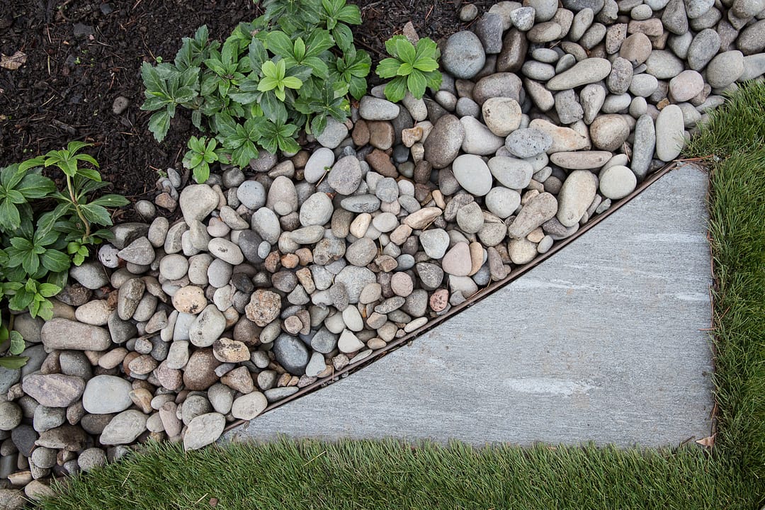 Edge of concrete paver with river rock and grass alongside