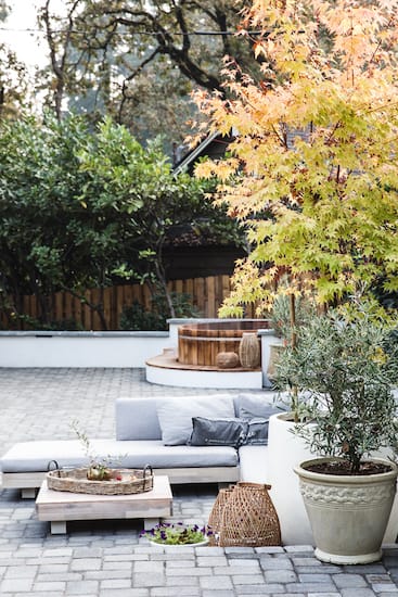 Large patio with paver flooring and retaining walls with outdoor furniture and large potted plants